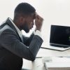 Stressed african businessman sitting in office with hand on forehead